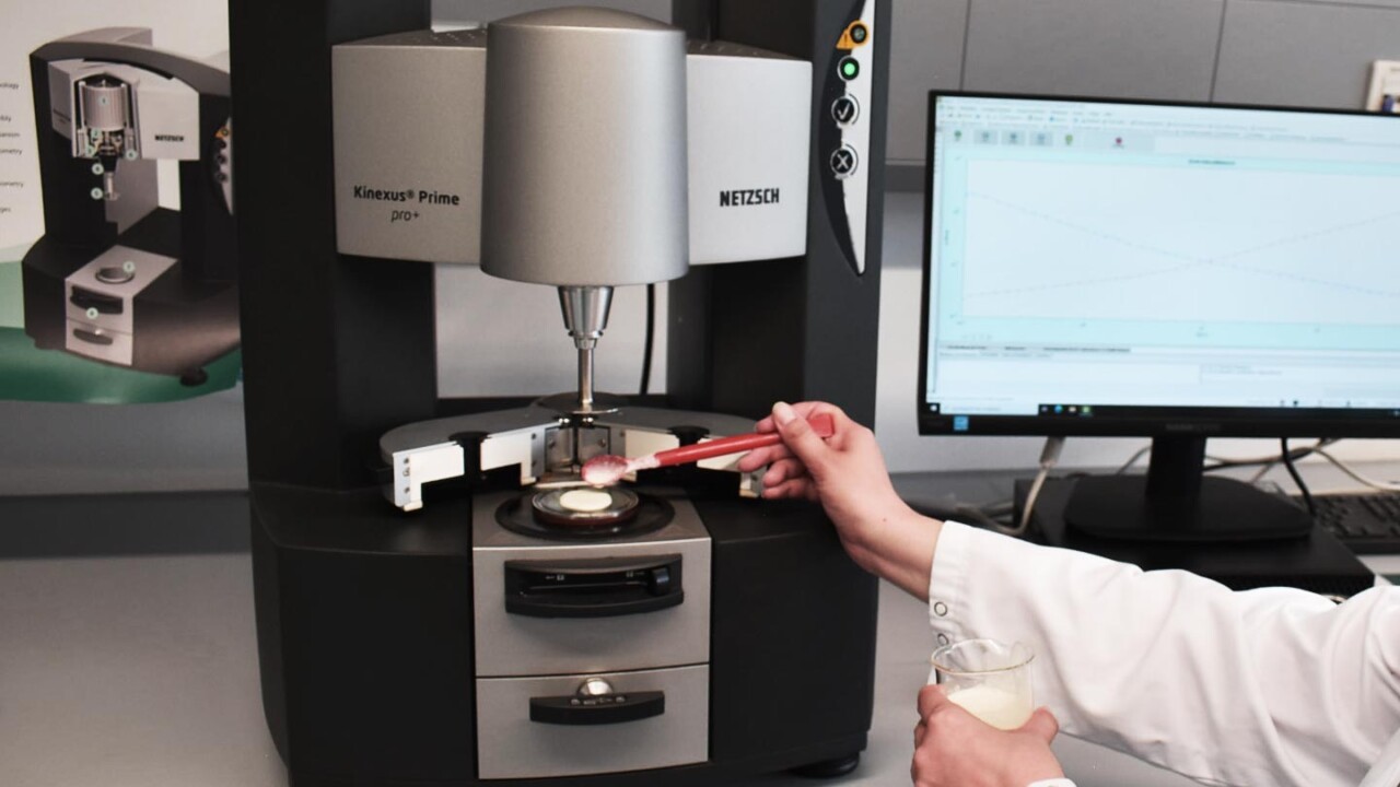 Laboraufnahme eines Rheometers (NETZSCH Kinexus Prime). Eine Person im Laborkittel bringt mit einem Spatel eine Probe auf die Messgeometrie auf, während am Monitor die Messkurve angezeigt wird. Das Bild steht für rheologische Analytik und die Charakterisierung von Textur, Viskosität und Struktur-Eigenschaften von Lebensmitteln am Zentrum für Lebensmittelphysik (ZLP).