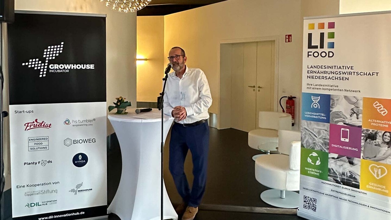 Ein Referent spricht an einem Stehtisch in einen Mikrofonständer bei einer Veranstaltung im Growhouse Incubator. Neben ihm stehen Roll-up-Banner von „Growhouse Incubator“ und „LiFOOD – Landesinitiative Ernährungswirtschaft Niedersachsen“ mit Themen wie Lebensmittelverarbeitung, Digitalisierung, alternative Proteine und gesunde Ernährung. Das Bild zeigt Networking und Wissenstransfer im Innovationshub des DIL.