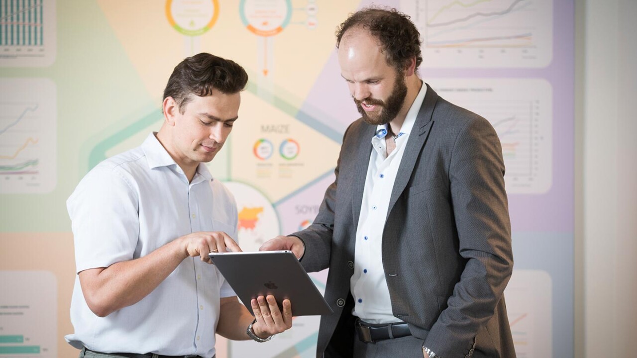 Zwei Mitarbeitende stehen im Büro und besprechen Inhalte auf einem Tablet. Im Hintergrund sind Diagramme und Visualisierungen zu Datenanalysen zu sehen. Das Bild steht für Food Data Analytics, Digitalisierung, datengetriebene Entscheidungsunterstützung, Projektarbeit und Beratung – z. B. für Nachhaltigkeit, Prozessoptimierung und Wertschöpfung in der Lebensmittelwirtschaft.