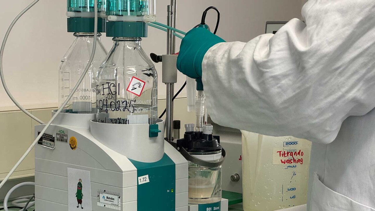 Laboraufnahme einer automatisierten Titrationsanlage: Eine Person im Laborkittel und mit Handschuhen bedient ein Messsystem mit Reagenzflaschen und Elektroden. Die Probe wird in einem Becherglas gerührt und analysiert. Das Bild steht für quantitative chemische Analytik, Qualitätskontrolle und biochemische Untersuchungen – z. B. zur Bestimmung von Säuregehalt, pH-Wert oder weiteren Parameter in Lebensmitteln und Prozessmedien.