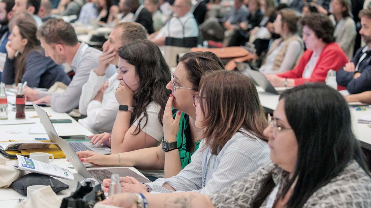 Teilnehmende sitzen in einem gut besuchten Kongresssaal und verfolgen aufmerksam das Programm. Im Vordergrund arbeiten mehrere Personen mit Laptops und Notizen, im Hintergrund ist das volle Publikum zu sehen. Die Szene vermittelt eine professionelle Tagungsatmosphäre mit Fokus auf Wissenstransfer, Diskussionen und Networking rund um Insekten als innovative Proteinquelle und Anwendungen in der Lebensmittelwirtschaft.